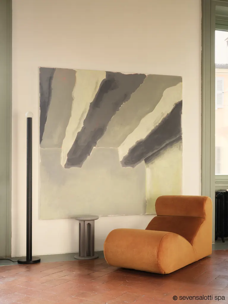 Poltrona Boborelax Arflex color arancio su pavimento in cotto, davanti a un grande quadro astratto