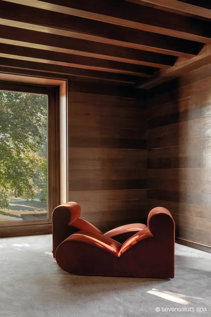 Poltrona Boborelax Arflex rosso scuro in una stanza rivestita in legno con grande finestra sul giardino