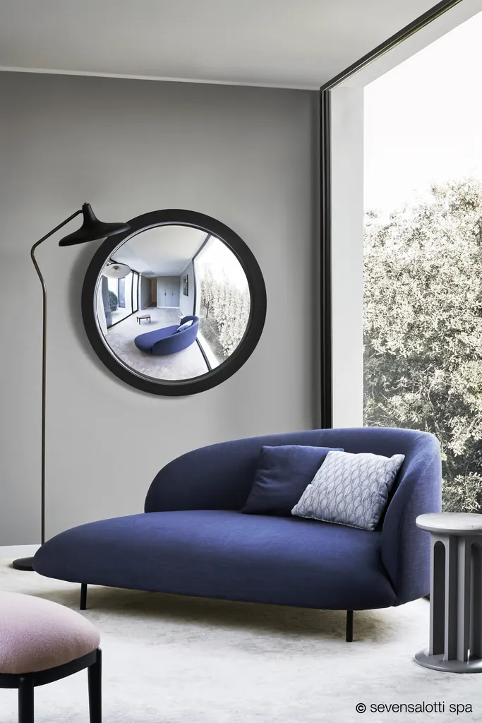 Divano Bonsai Arflex blu con piedi in metallo accanto a uno specchio rotondo e a una vetrata