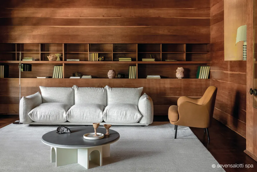Poltrona Brigitte Arflex color cuoio accanto a un divano bianco, in un soggiorno con pareti e libreria in legno