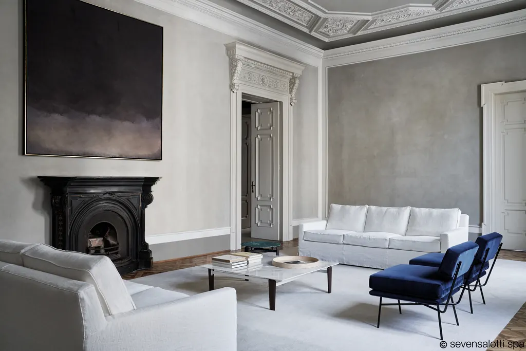 Divano e poltrona Cousy Arflex bianchi in un salone classico con camino e soffitto a stucchi