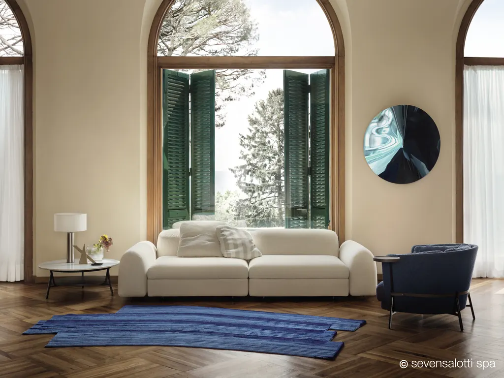 Divano Edo Arflex bianco con tappeto blu davanti a una finestra ad arco con persiane verdi