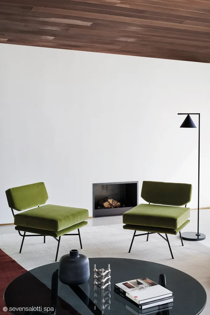 Due poltrone Elettra Arflex verdi davanti a un camino, con soffitto in legno e lampada da terra nera