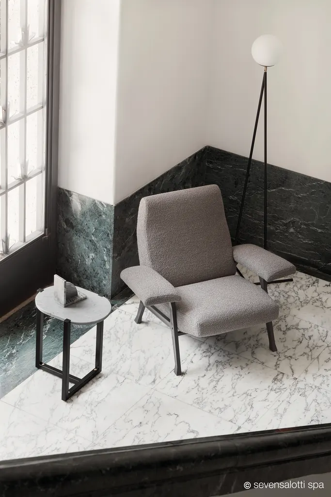 Poltrona Hall Arflex grigia con base scura su un pavimento in marmo, accanto a una finestra