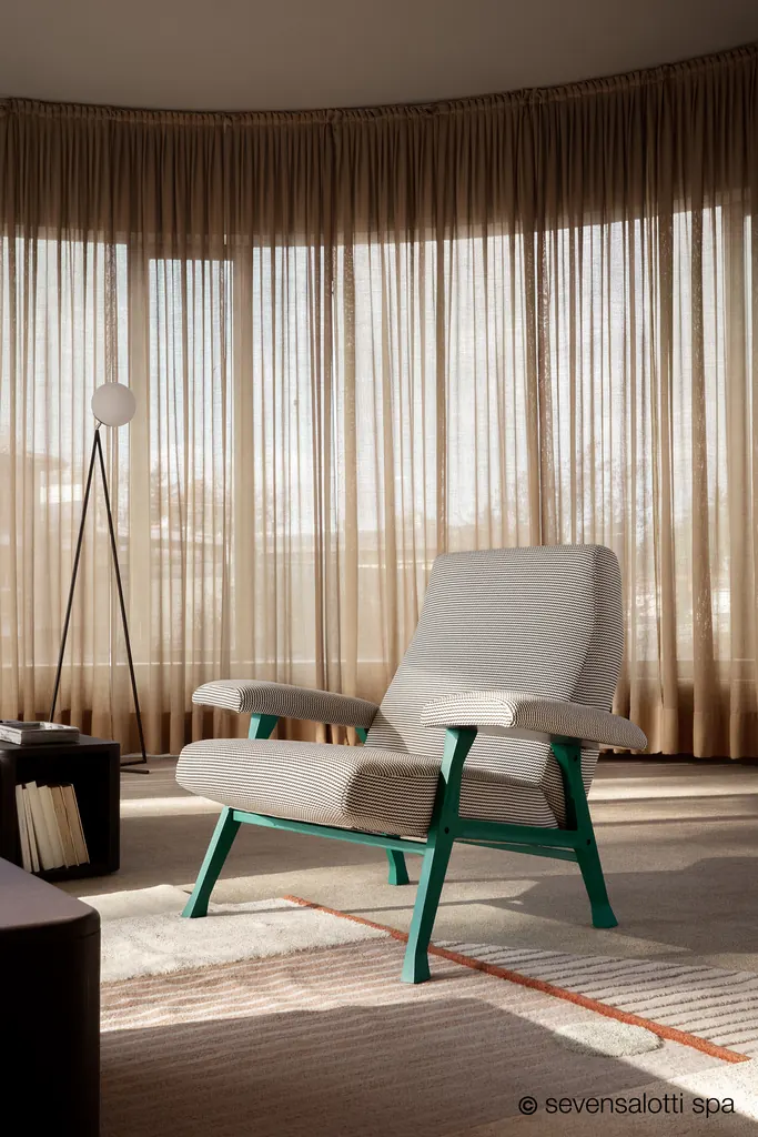 Poltrona Hall Arflex grigio chiaro con base verde in una sala con tende e lampada da terra