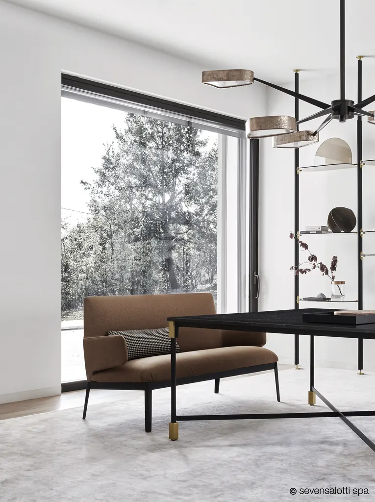 Love seat Hug Arflex marrone accanto a una scrivania nera davanti a una vetrata