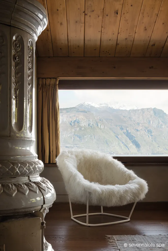 Poltrona Katrin Arflex in pelliccia bianca accanto a una stufa in maiolica e a una finestra sulle montagne
