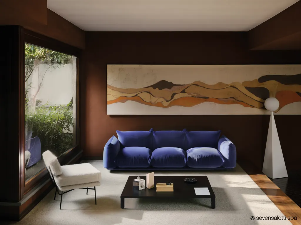Blue Marenco Arflex sofa in a living room with brown walls and a large window onto the garden