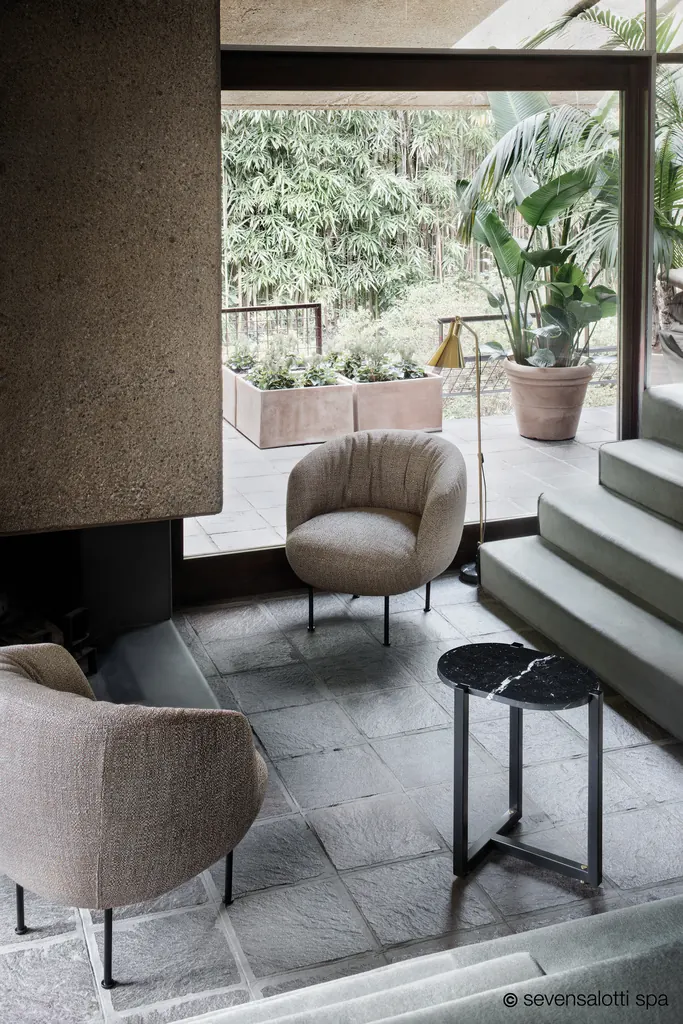 Due poltrone Supplì Arflex beige su un pavimento in pietra, con tavolino in marmo nero e giardino sullo sfondo