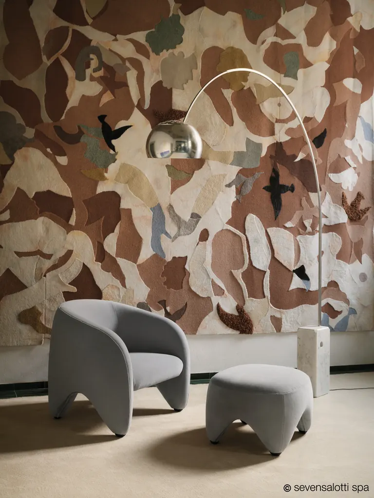 Poltrona Yuzu Arflex grigia con pouf sotto una lampada ad arco, davanti a un arazzo