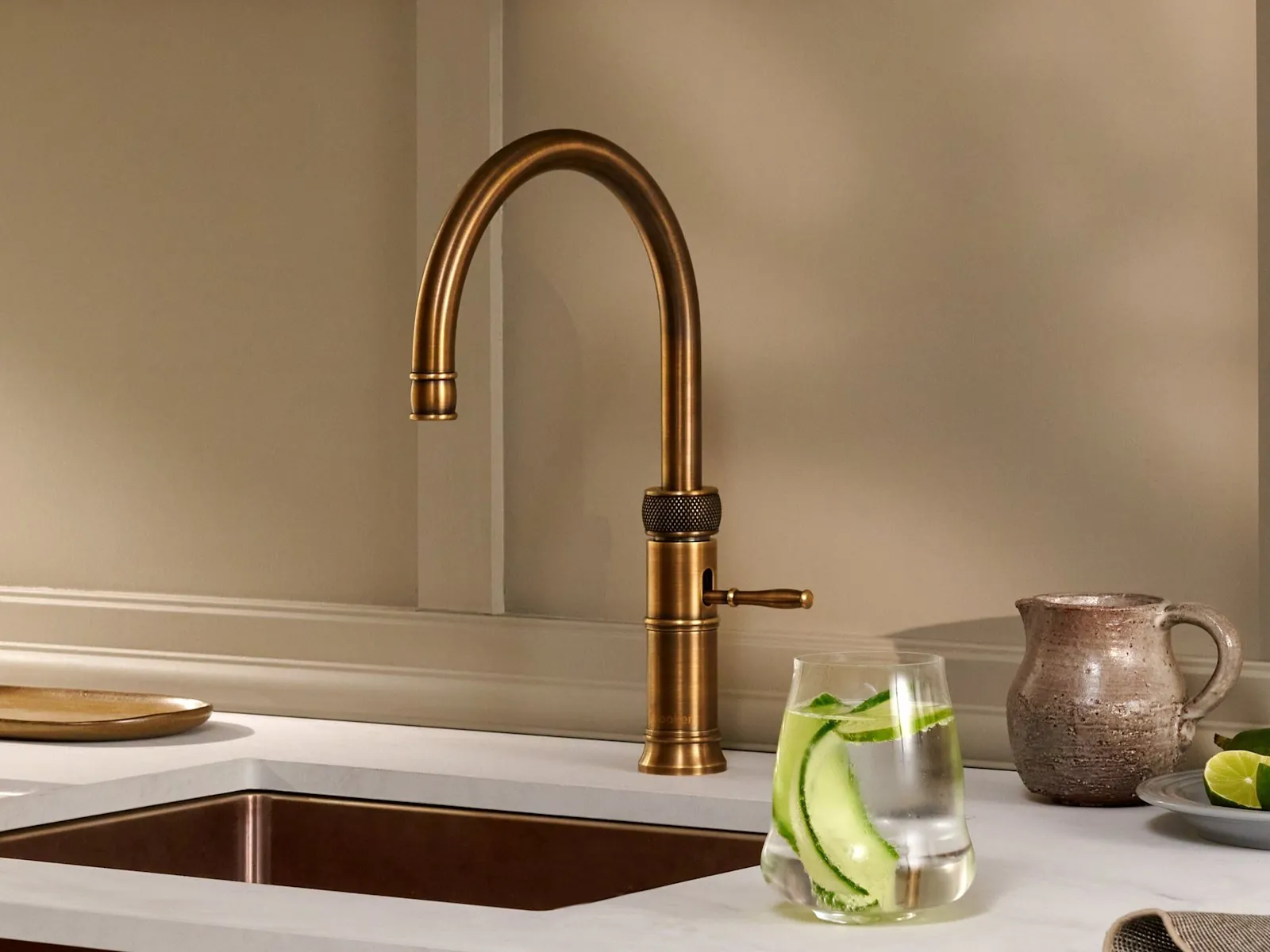 Rubinetto Quooker Classic Fusion Round in ottone patinato su un piano cucina chiaro, con un bicchiere di acqua frizzante