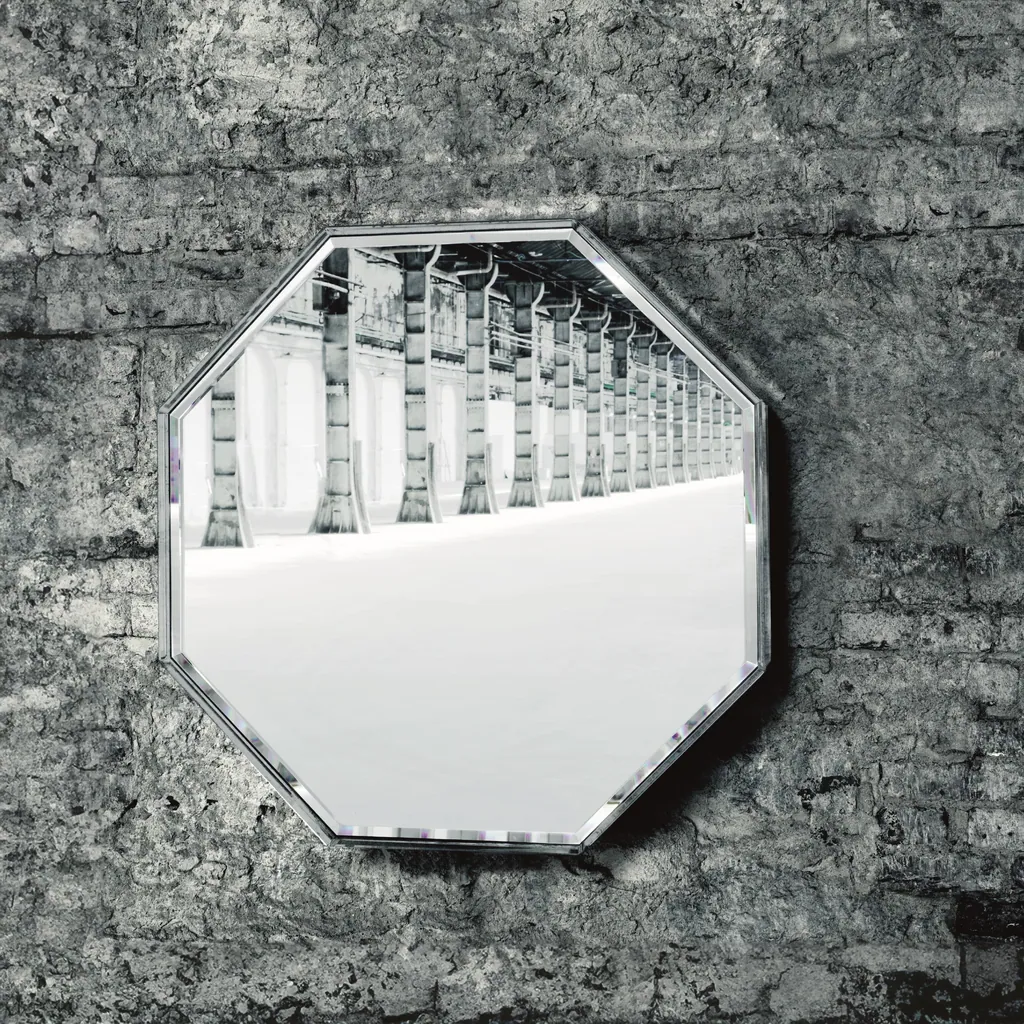Specchio ottagonale Prism Mirror di Glas Italia su una parete di mattoni grigi