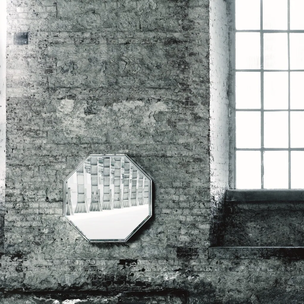 Specchio ottagonale Prism Mirror di Glas Italia in un ambiente industriale, accanto a una finestra